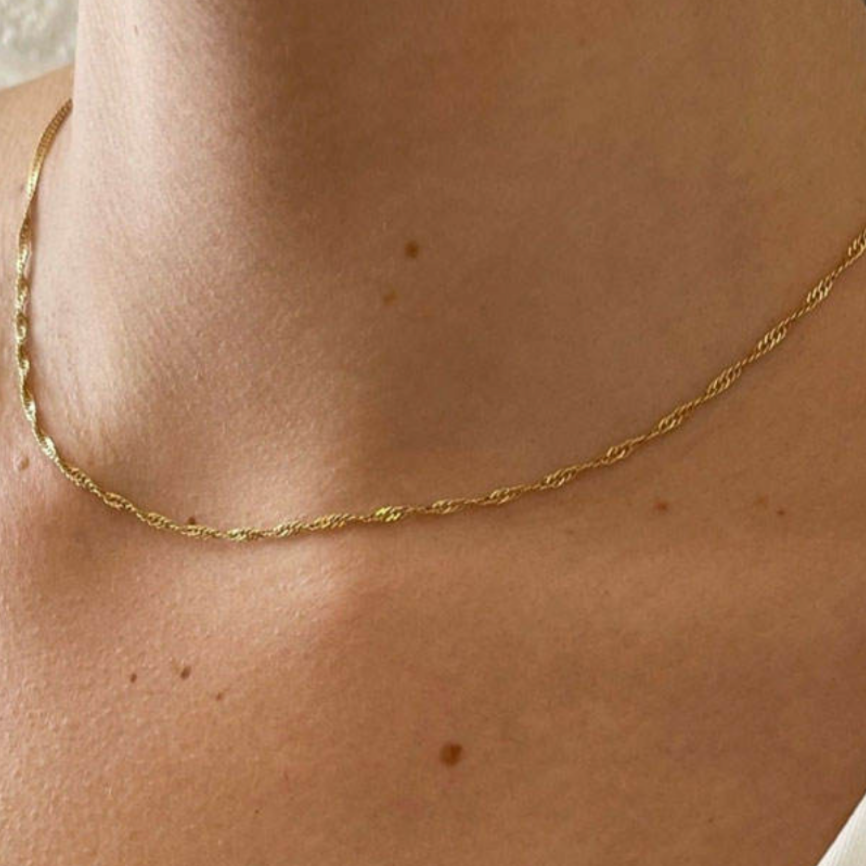 Gold necklace on a person's neck with a neutral background